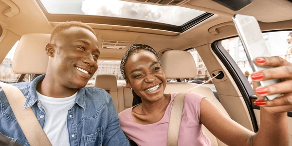 A happy young couple leaning against their new car while looking at a smartphone